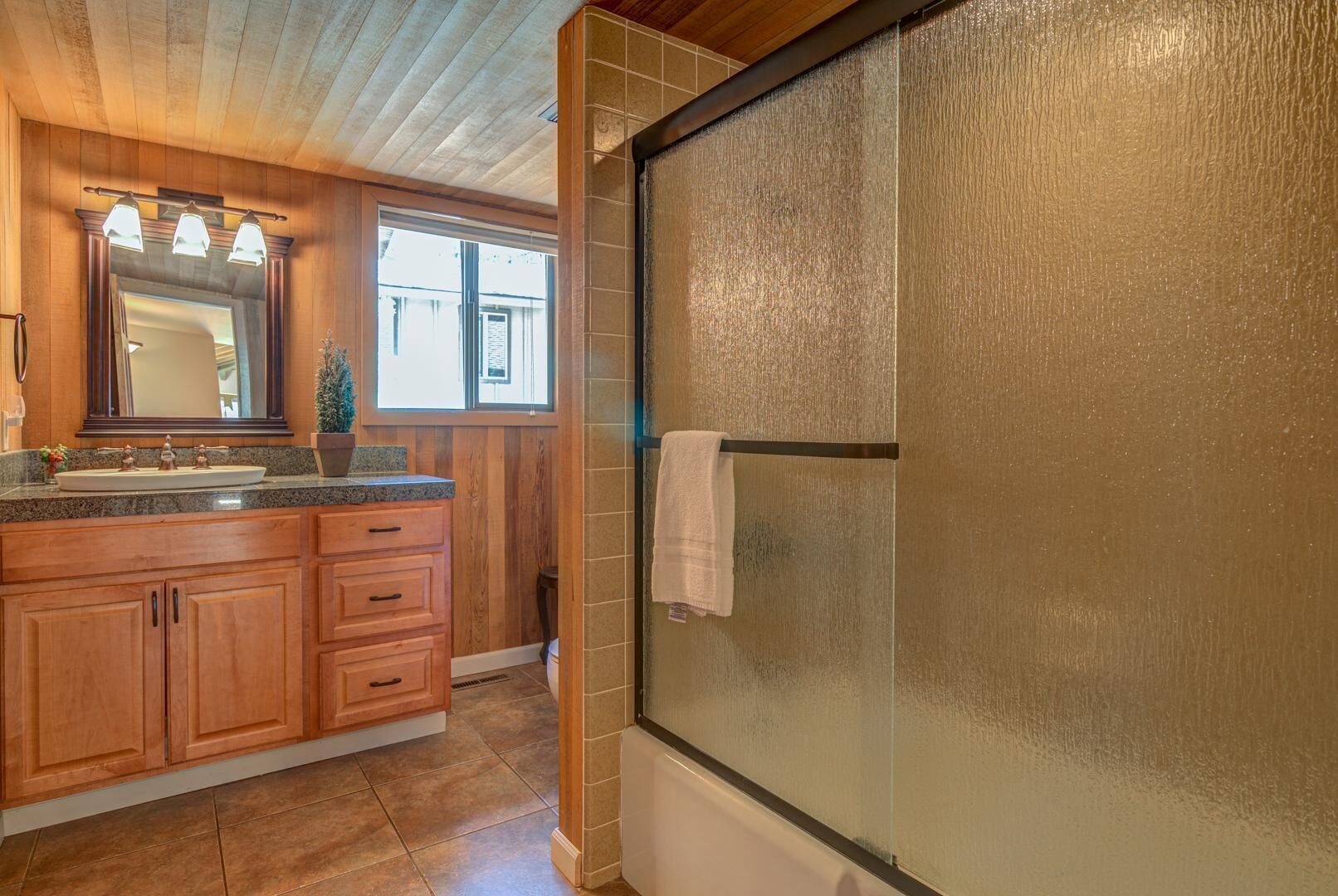 A bathroom with a glass shower door, wooden cabinets, and a large mirror.