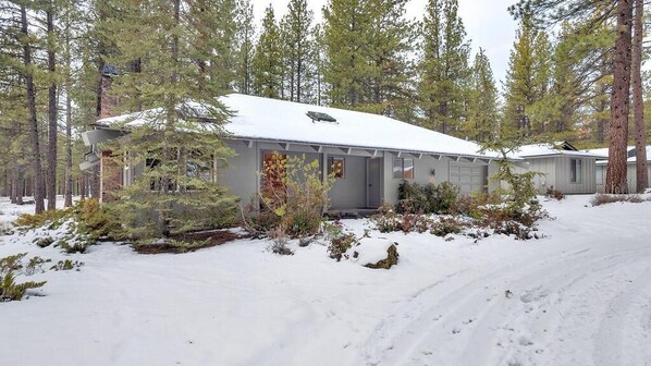 A single-story cabin with a snow-covered roof, surrounded by tall pine trees. - Quartz Mt. Lane 1 (Bend)