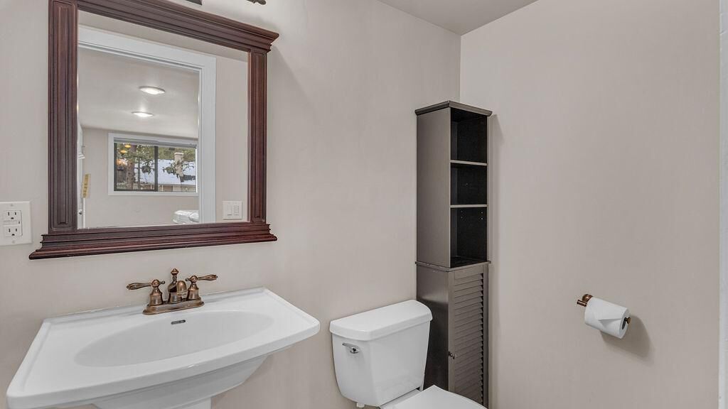 Un baño con un lavabo blanco, un inodoro, un espejo con marco de madera y una estantería.