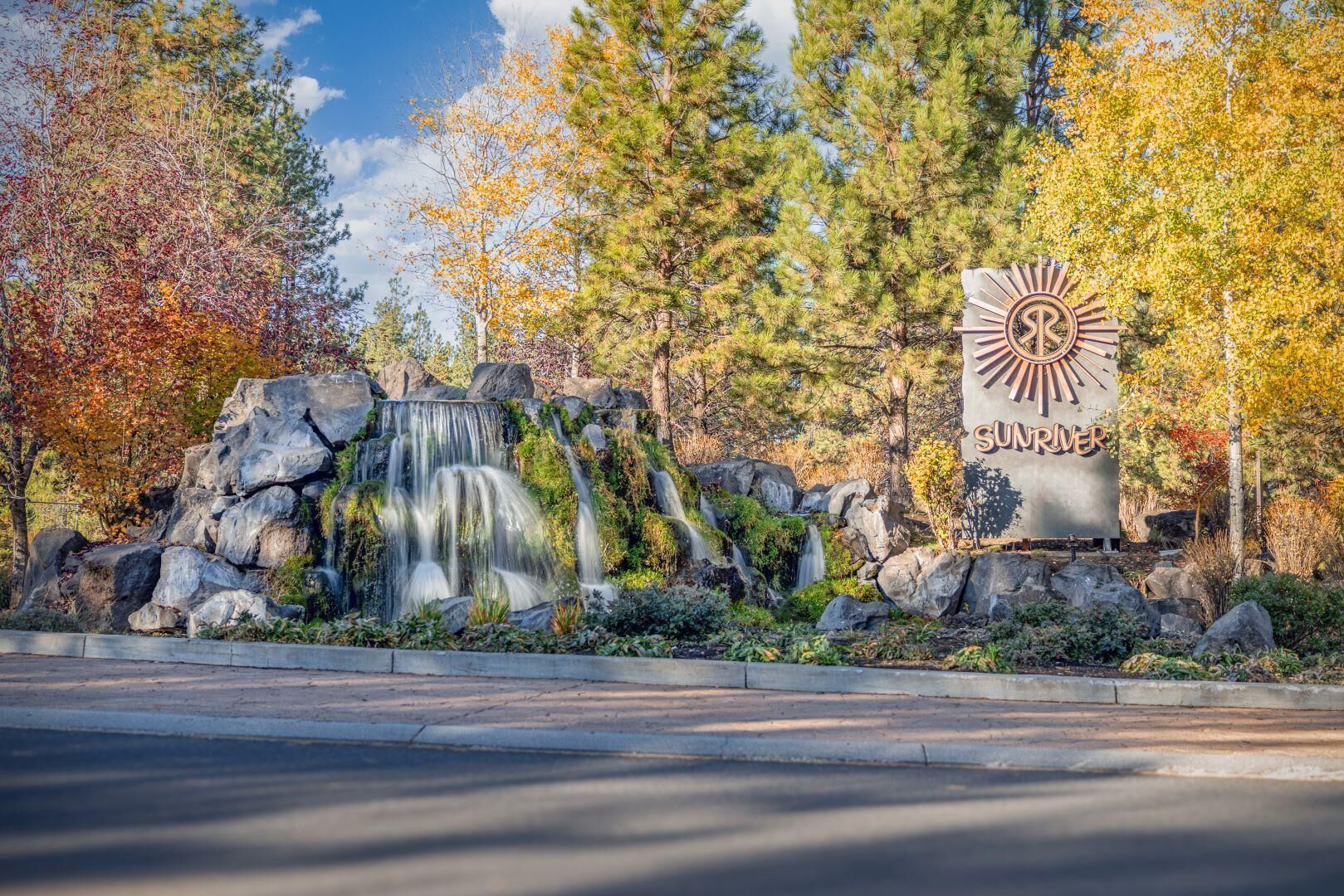 A waterfall feature with a sign reading "SUNRIVER" in a natural setting with trees and rocks.