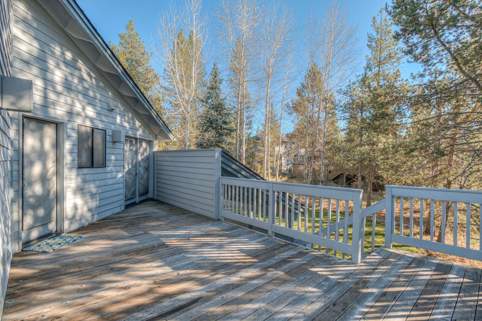 A wooden deck with a white railing, adjacent to a house with a garage door and a window.
