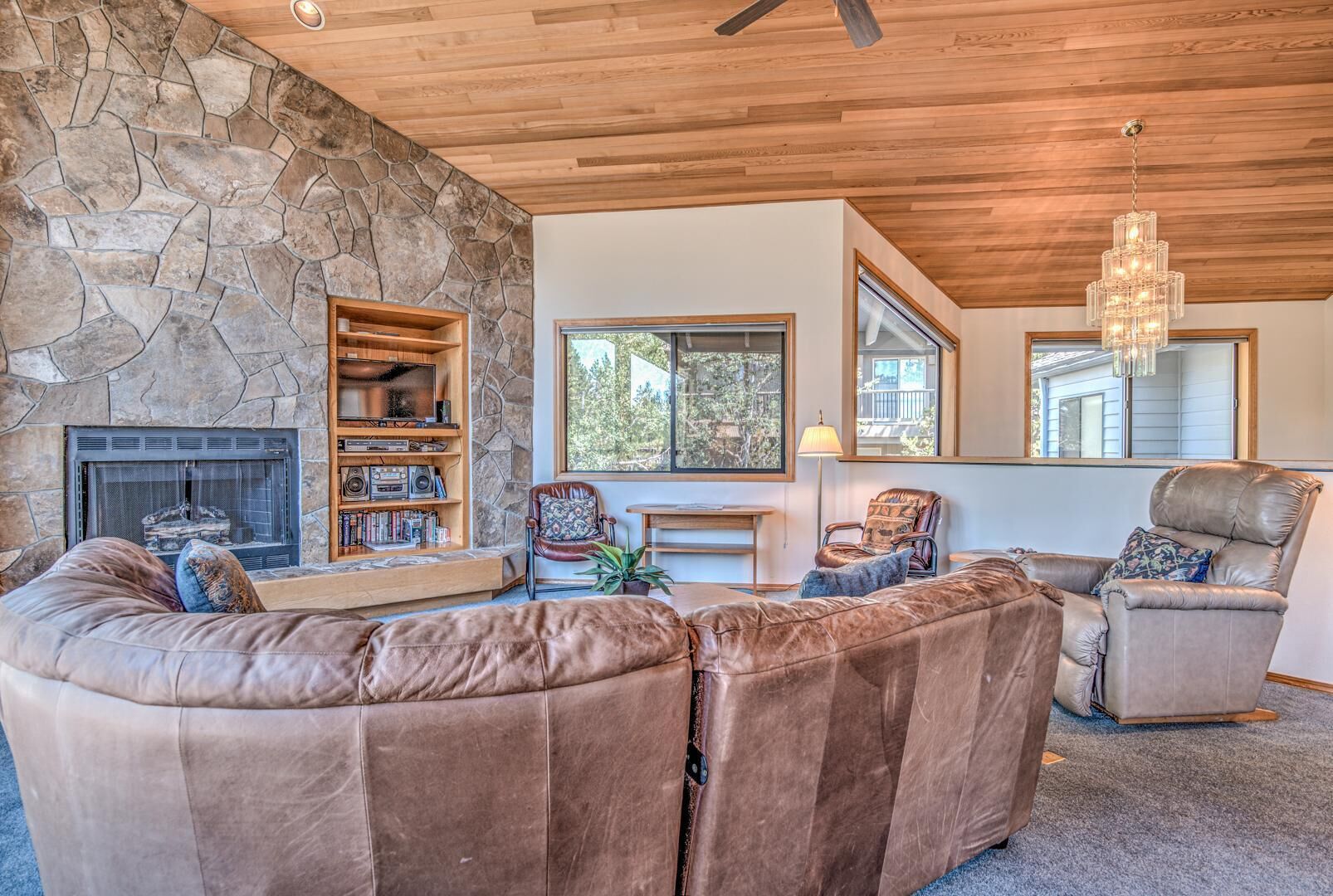 A cozy living room with a stone wall, leather sofas, a fireplace, and a large window offering a view of trees.