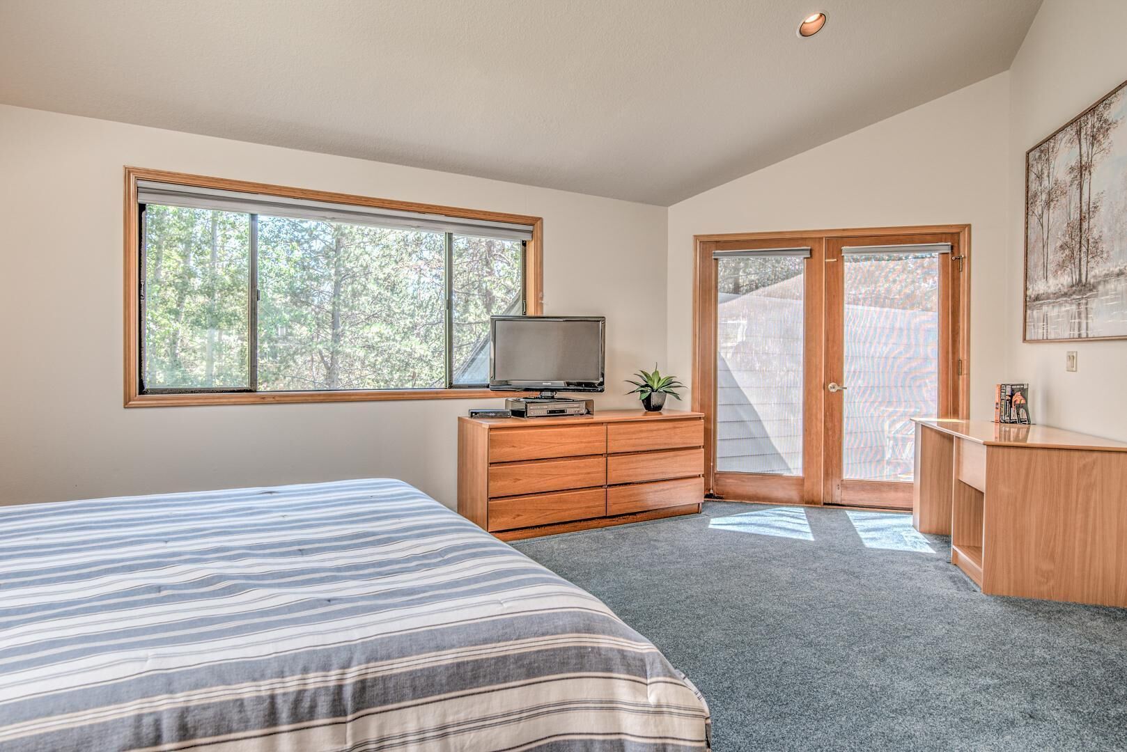 Un dormitorio con cama, cómoda, televisor y ventana grande.