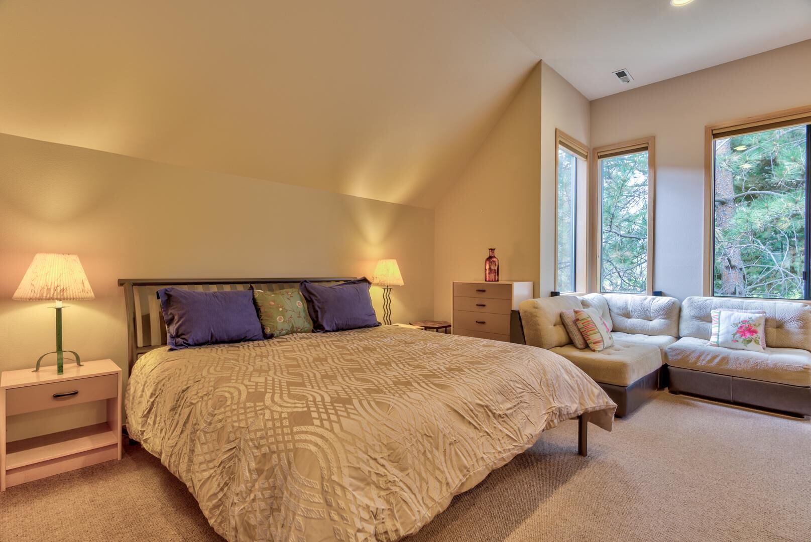 Camera da letto con un letto grande, un comodino, una cassettiera e un angolo salotto con divano e poltrone. Due finestre offrono luce naturale e vista sugli alberi.