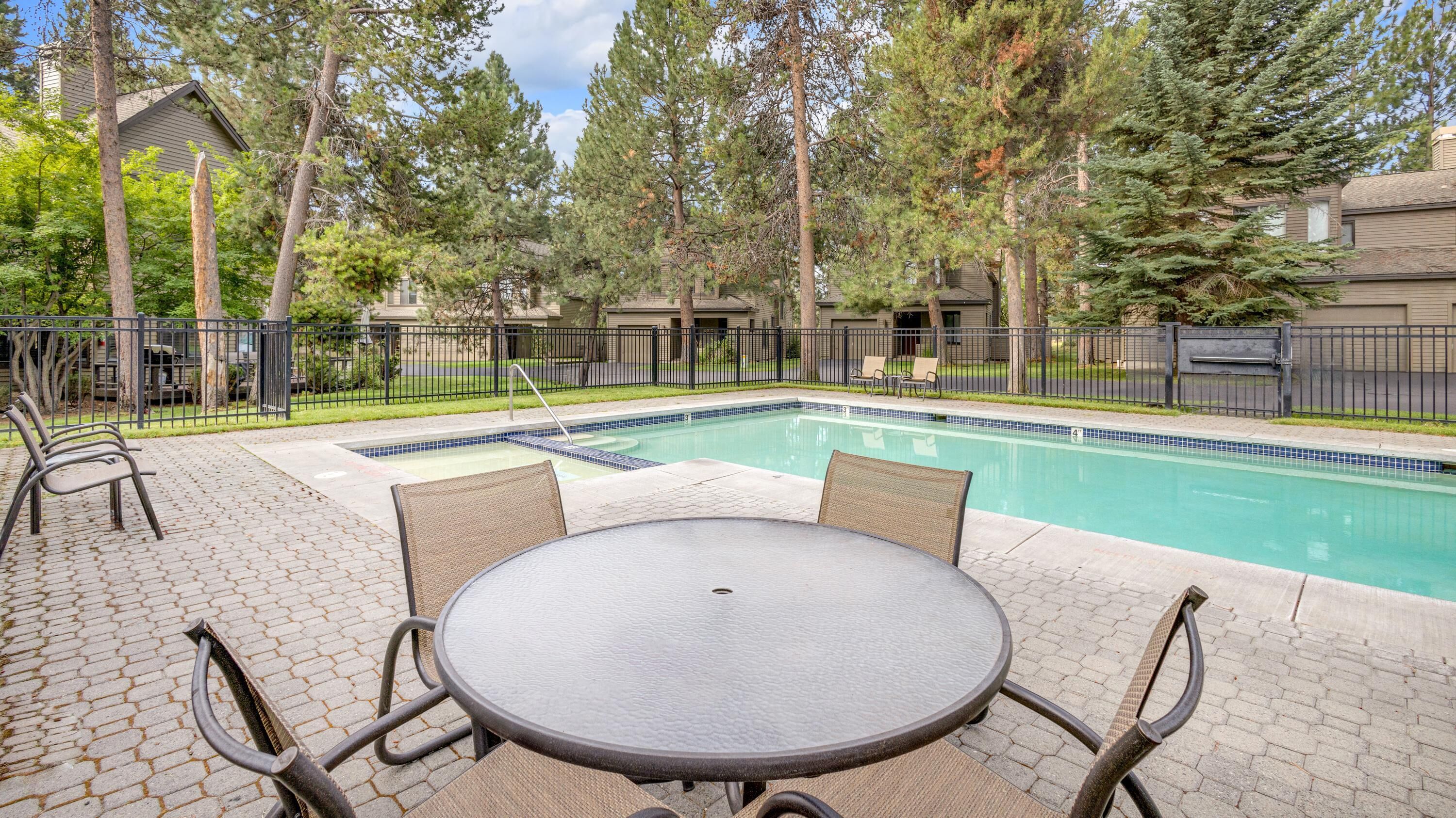 A pool area with a rectangular pool, surrounded by a paved patio with a round table and chairs.