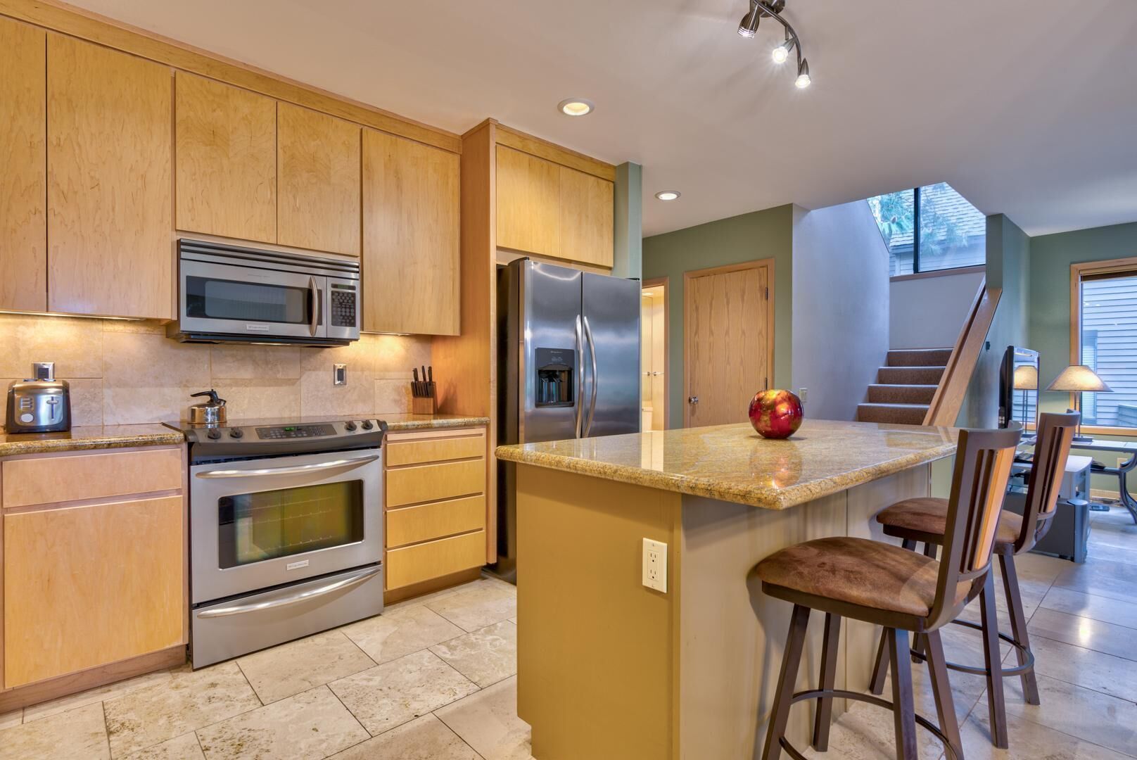 A modern kitchen with wooden cabinets, stainless steel appliances, a granite countertop, and a small island with bar stools.