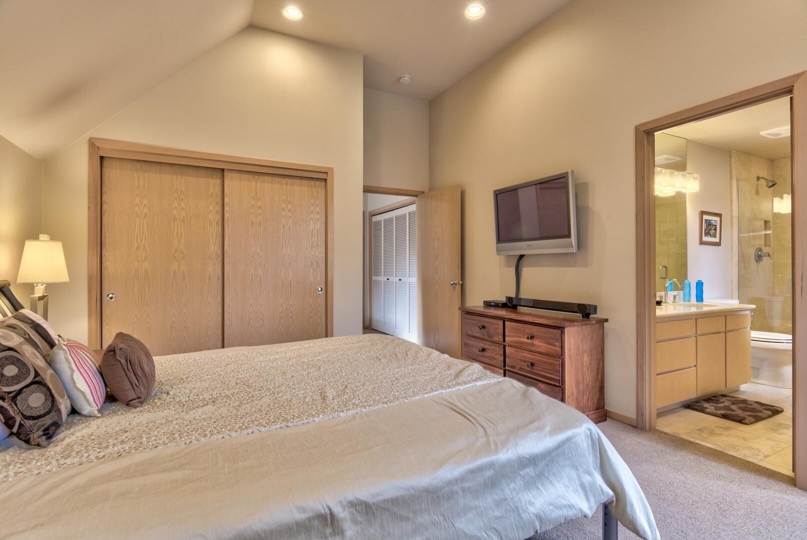 A bedroom with a large bed, wooden wardrobe, a television, and a bathroom visible through an open door.