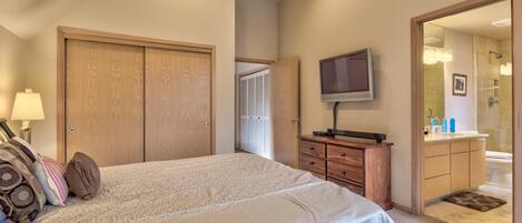 A bedroom with a large bed, wooden wardrobe, a television, and a bathroom visible through an open door.