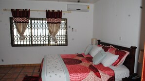 A bedroom with a bed, curtains, an air conditioning unit, and a window with a metal grille. - Madison Executive Guesthouse (Accra)