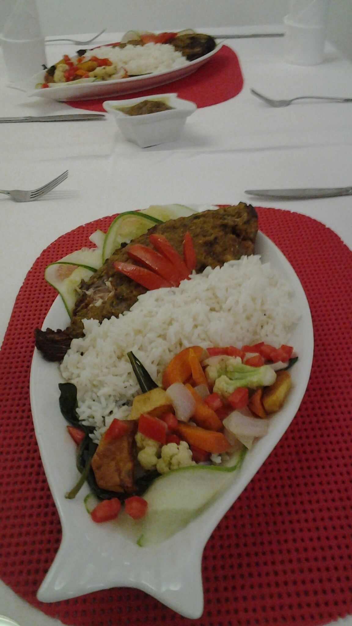A plate of food with rice, vegetables, and meat, placed on a red mat.