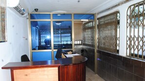 A reception area with a wooden reception desk, a computer, and a chair. There is a window with a metal grille and a sign that reads "MANAGER". - Madison Executive Guesthouse (Accra)