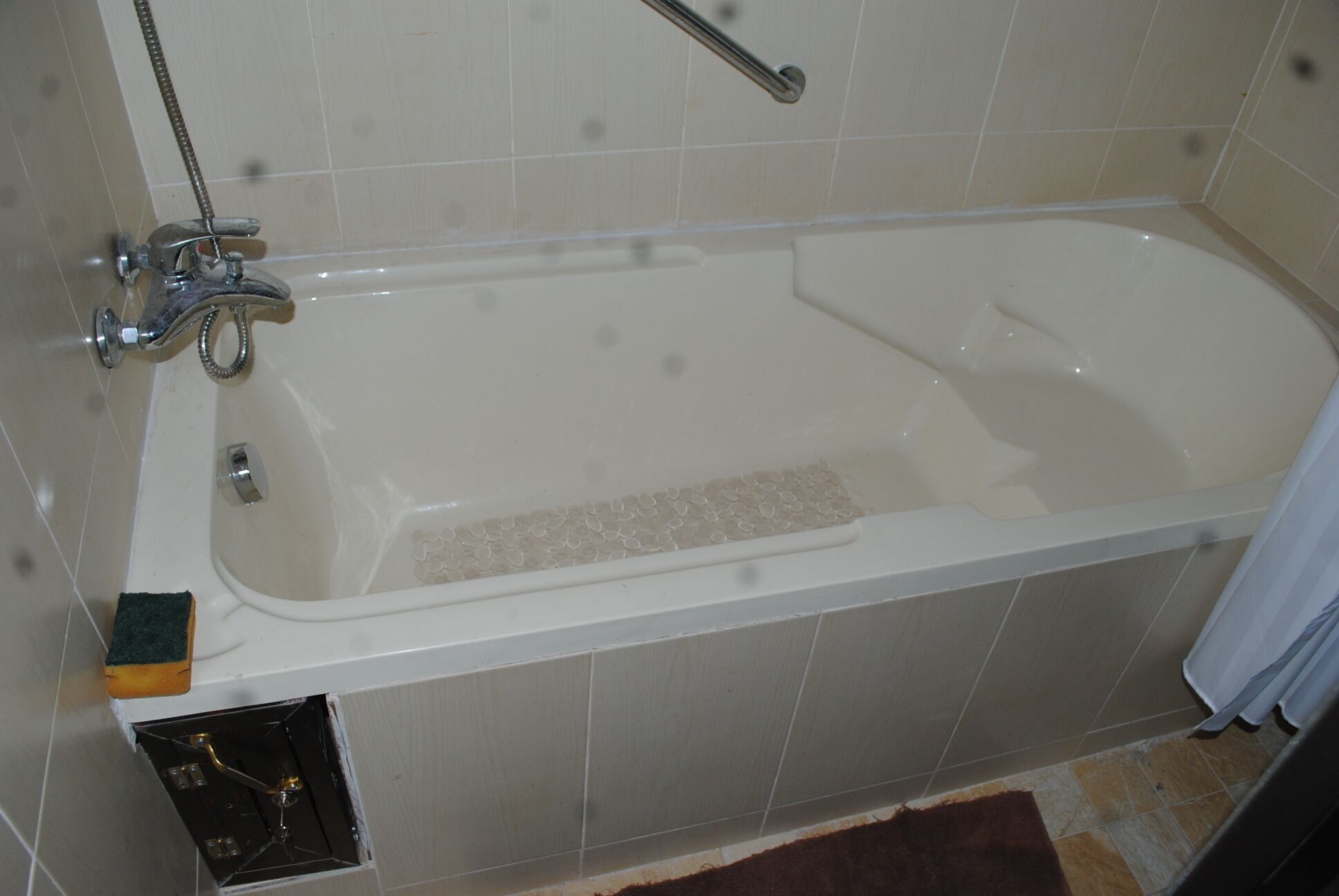 A standard bathtub with a handheld showerhead and a handheld faucet.