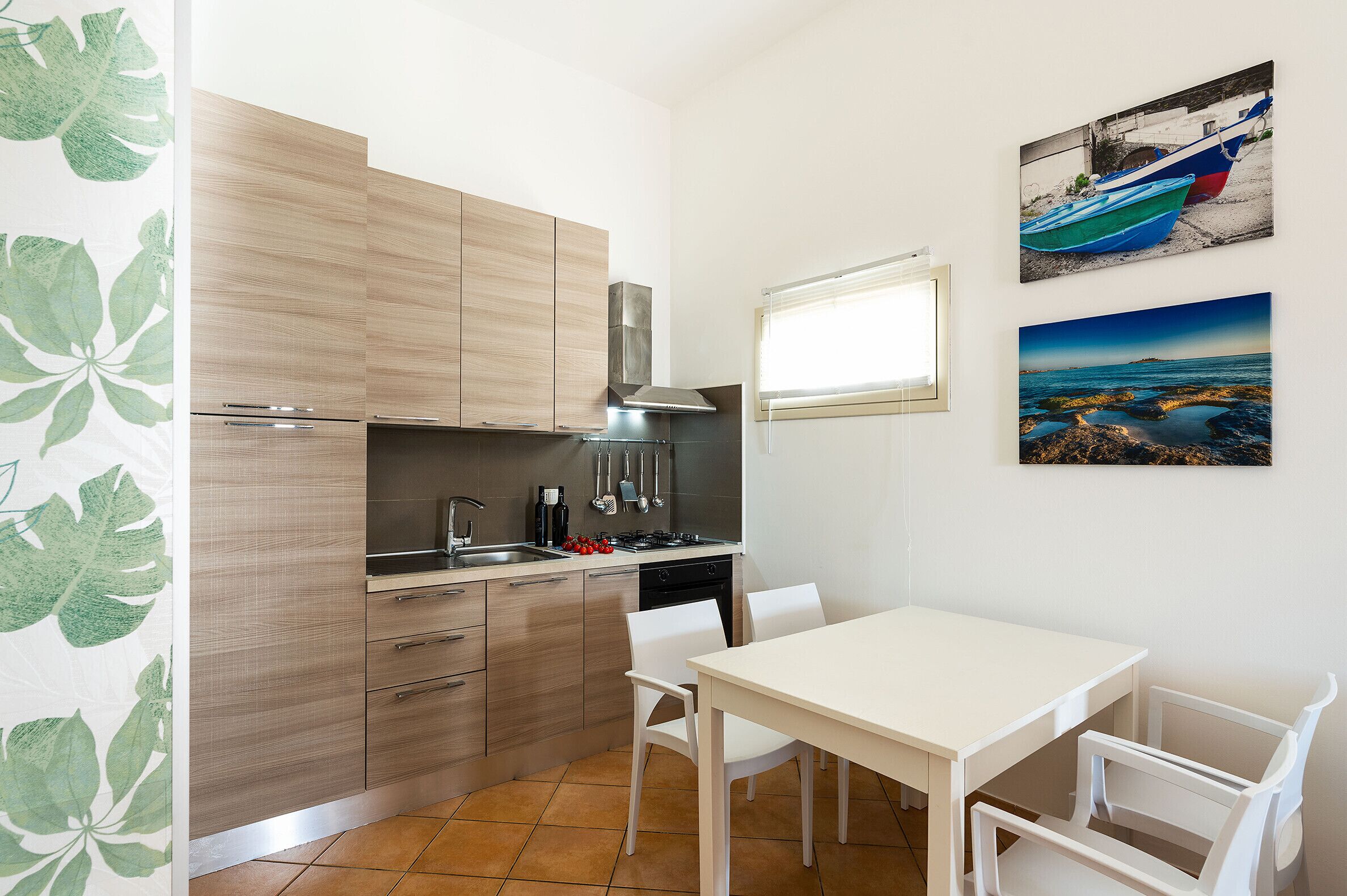 Eine kompakte Küche mit Holzausstattung, einem weißen Esstisch und Stühlen. An der Wand befinden sich zwei gerahmte Bilder.