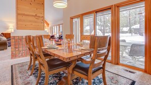 A dining area with a wooden table and chairs, large windows, and a view of the outdoors. - Awbrey Lane #7 by Village Properties at Sunriver (Bend)