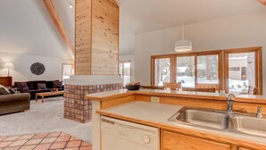 A modern kitchen with a wooden island, a built-in dishwasher, and a large window with a view of a snowy landscape. - Awbrey Lane #7 by Village Properties at Sunriver (Bend)