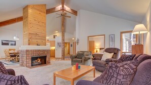 A cozy living room with a fireplace, wooden beams, and comfortable seating. - Awbrey Lane #7 by Village Properties at Sunriver (Bend)