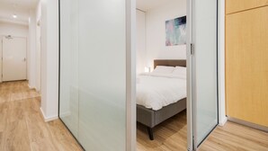 Quarto moderno com porta de vidro deslizante, cama com roupa de cama branca e piso de madeira.
