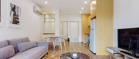 A modern living room with a sofa, a coffee table, a TV, and a dining area with chairs and a table.