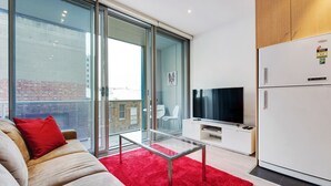 Un espacio habitable moderno con un sofá, una mesa de vidrio, una alfombra roja, un televisor y un refrigerador.