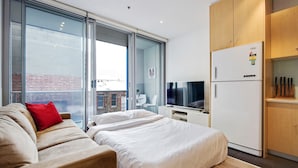 Una habitación de hotel moderna con sofá, dos camas, televisor, refrigerador y zona de cocina.
