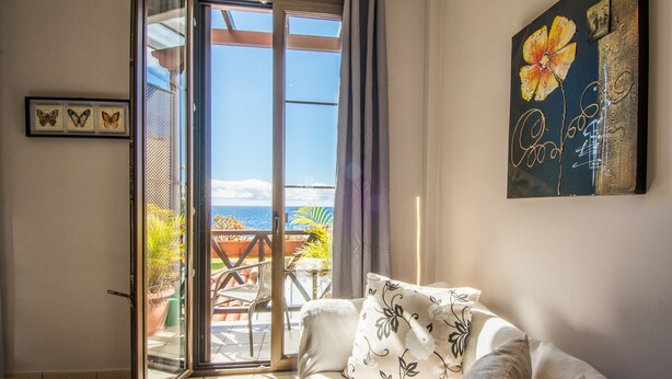 Ein Zimmer mit einer Schiebetür zum Balkon, einem Sofa mit gemusterten Kissen und einem gerahmten Kunstwerk an der Wand.