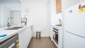 Una cocina moderna con armarios blancos, un lavavajillas de acero inoxidable, un bote de basura, un reloj y una estufa.
