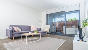 Una sala de estar moderna con un sofá gris, una mesa de centro y un televisor sobre un mueble blanco.