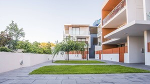 Un edificio residencial moderno de varios pisos con techo plano, un pequeño césped y un sendero pavimentado.