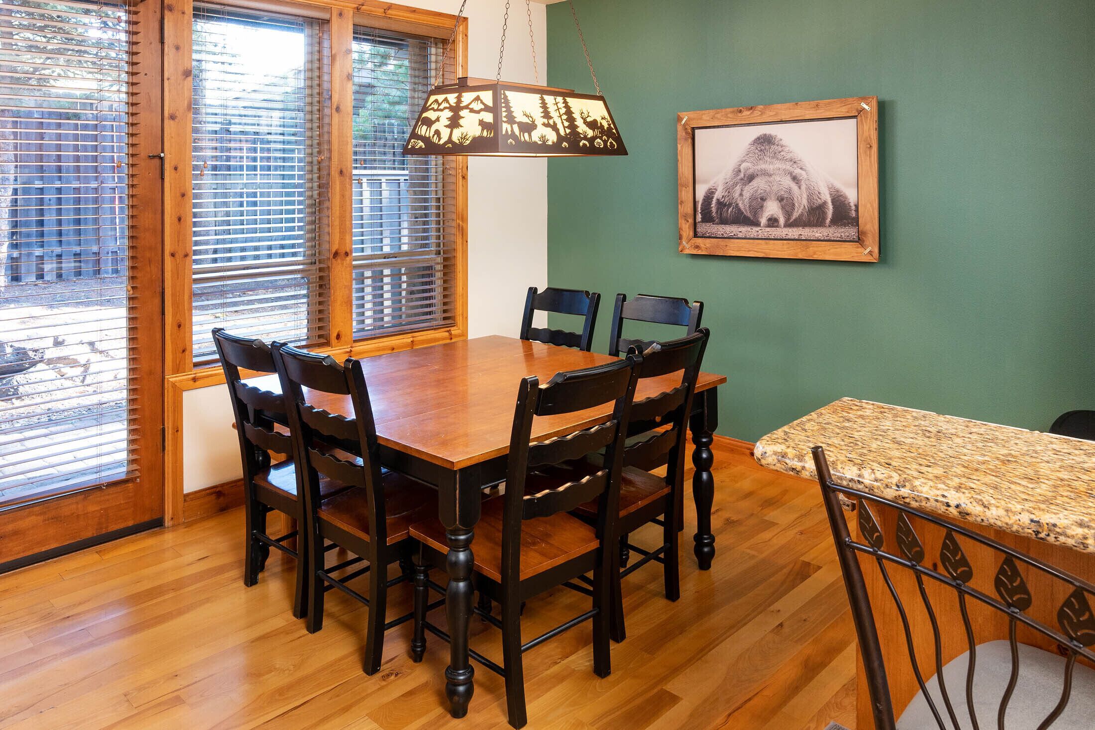 Uma área de refeições com mesa e cadeiras de madeira, luminária pendente e um quadro na parede.