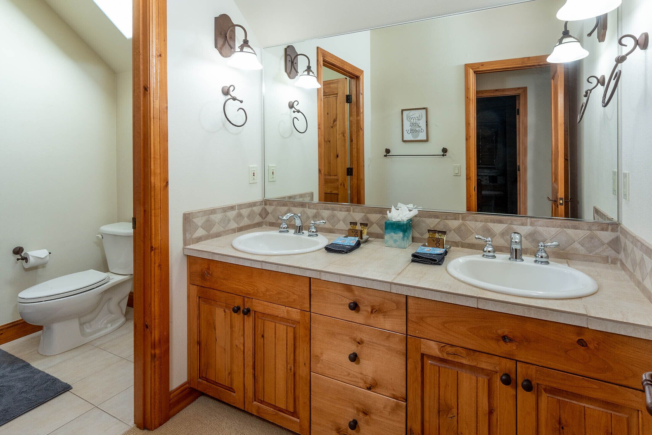 Baño con armarios de madera, dos lavamanos y un espejo grande.