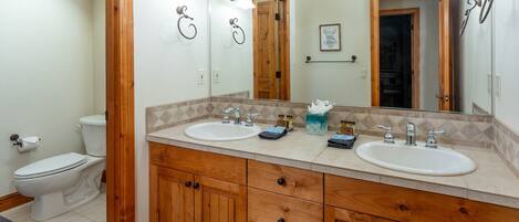Baño con armarios de madera, dos lavamanos y un espejo grande.