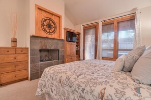 A bedroom with a bed, a fireplace, wooden cabinets, and a window with blinds.