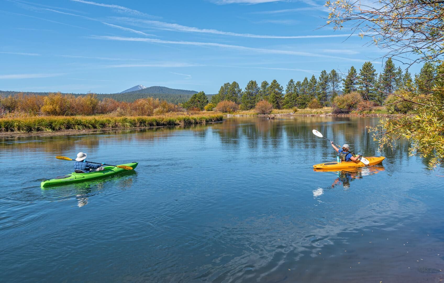 Two kayaks on a calm river with a forested landscape in the background.