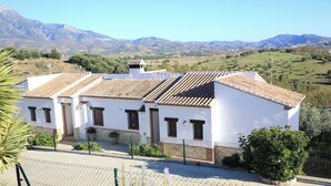 A white building with a tiled roof, surrounded by greenery and mountains. - Cozy Rural Tourism Accommodation in Huetor Spain (Vinuela)