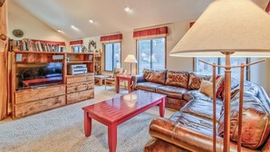 A cozy living room with a leather sofa, wooden coffee table, and a bookshelf filled with books. - Towhee Lane 5 (Bend)