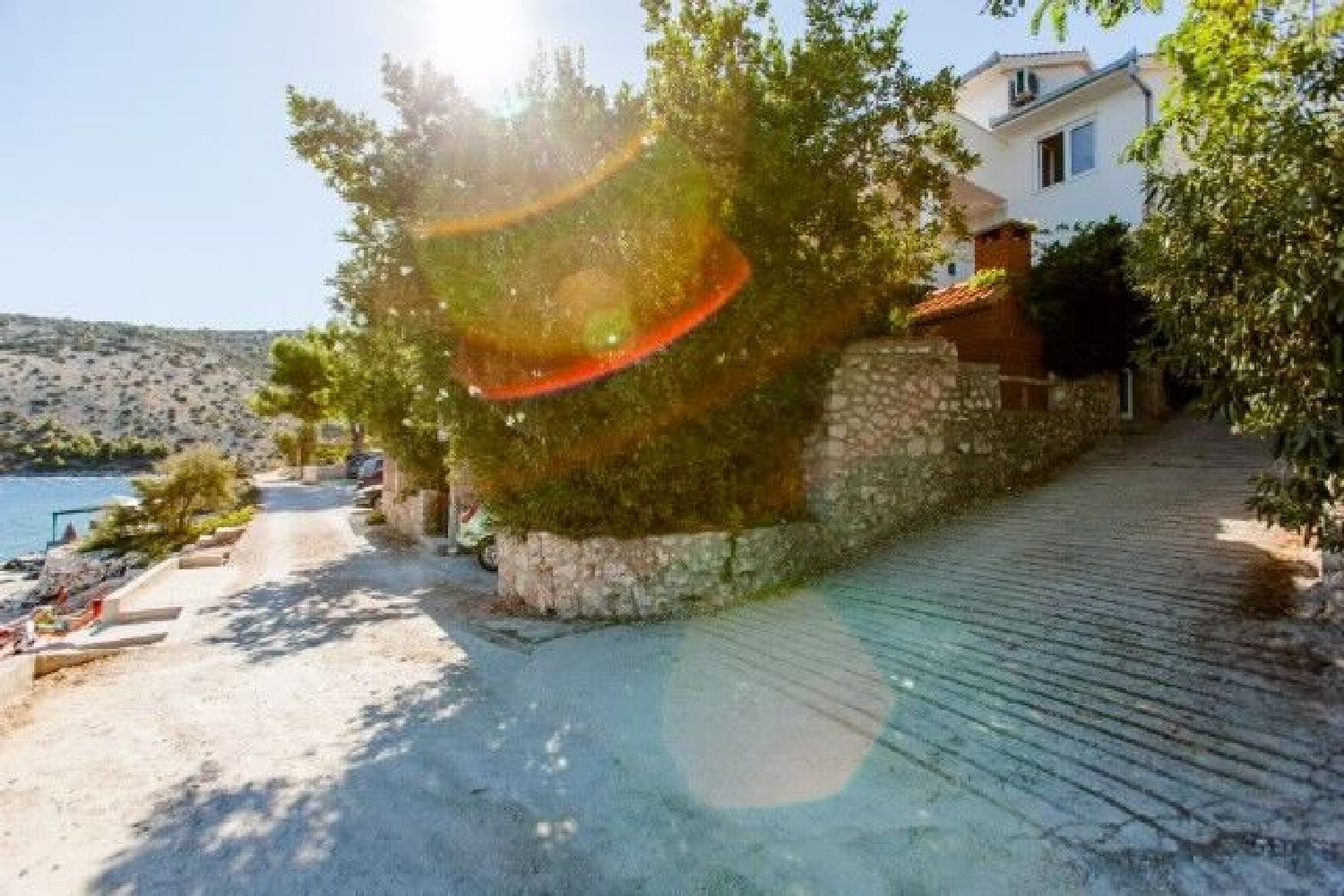 A coastal property with a paved walkway, stone walls, and a view of the sea.