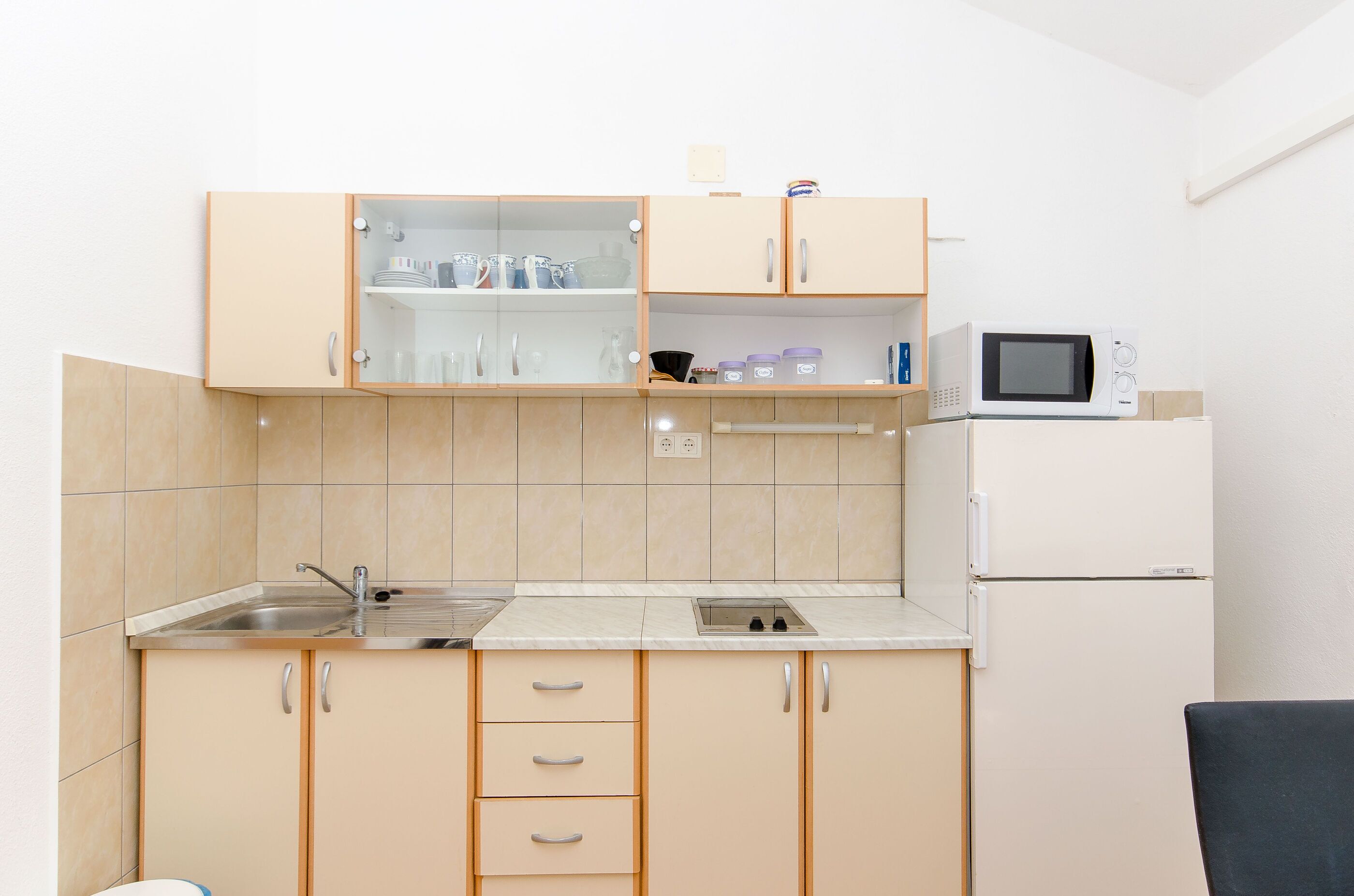 Eine kleine Küche mit Spüle, Schränken, einer Mikrowelle und einem Kühlschrank.