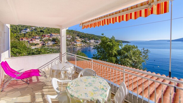 A balcony with a view of a coastal town, a table with chairs, and a pink lounge chair. - Apartments Ana (Vinisce)