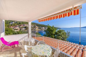 A balcony with a view of a coastal town, a table with chairs, and a pink lounge chair. - Apartments Ana (Vinisce)