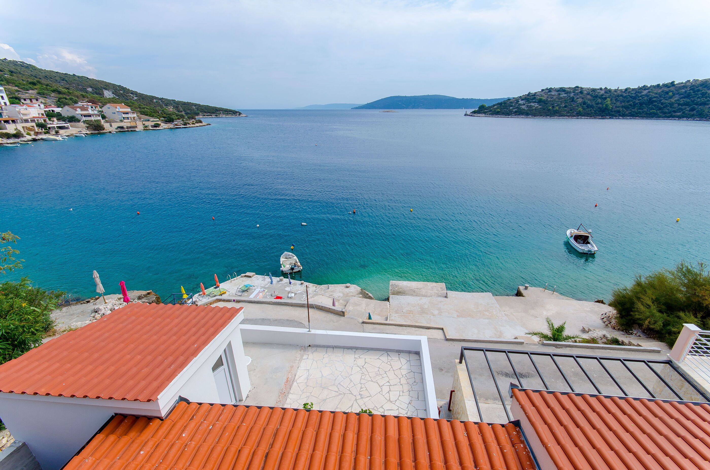 A coastal view with a clear blue sea, a small boat, and buildings on the shore.