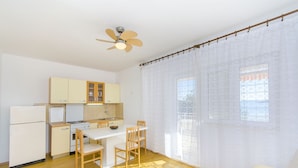A compact kitchen with wooden cabinets, a white refrigerator, a stove, and a dining table with chairs. - Apartments Ana (Vinisce)