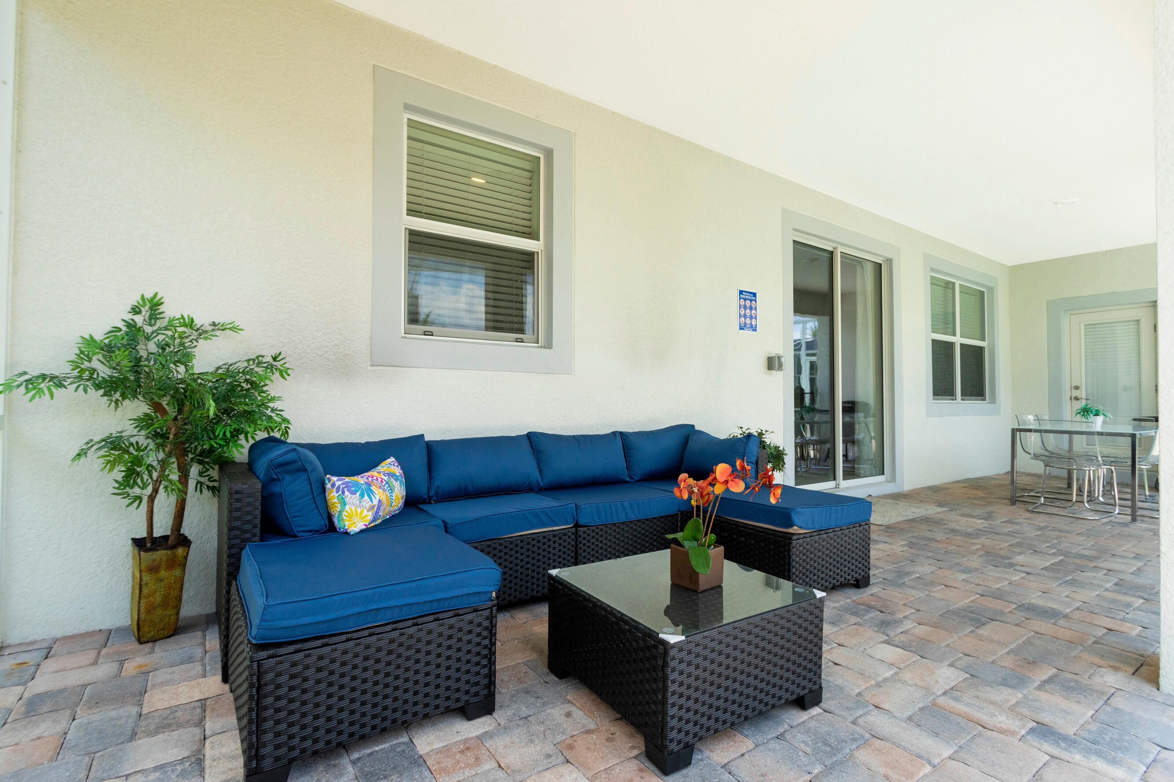 An outdoor seating area with a blue sofa, a glass-top table, and a potted plant.