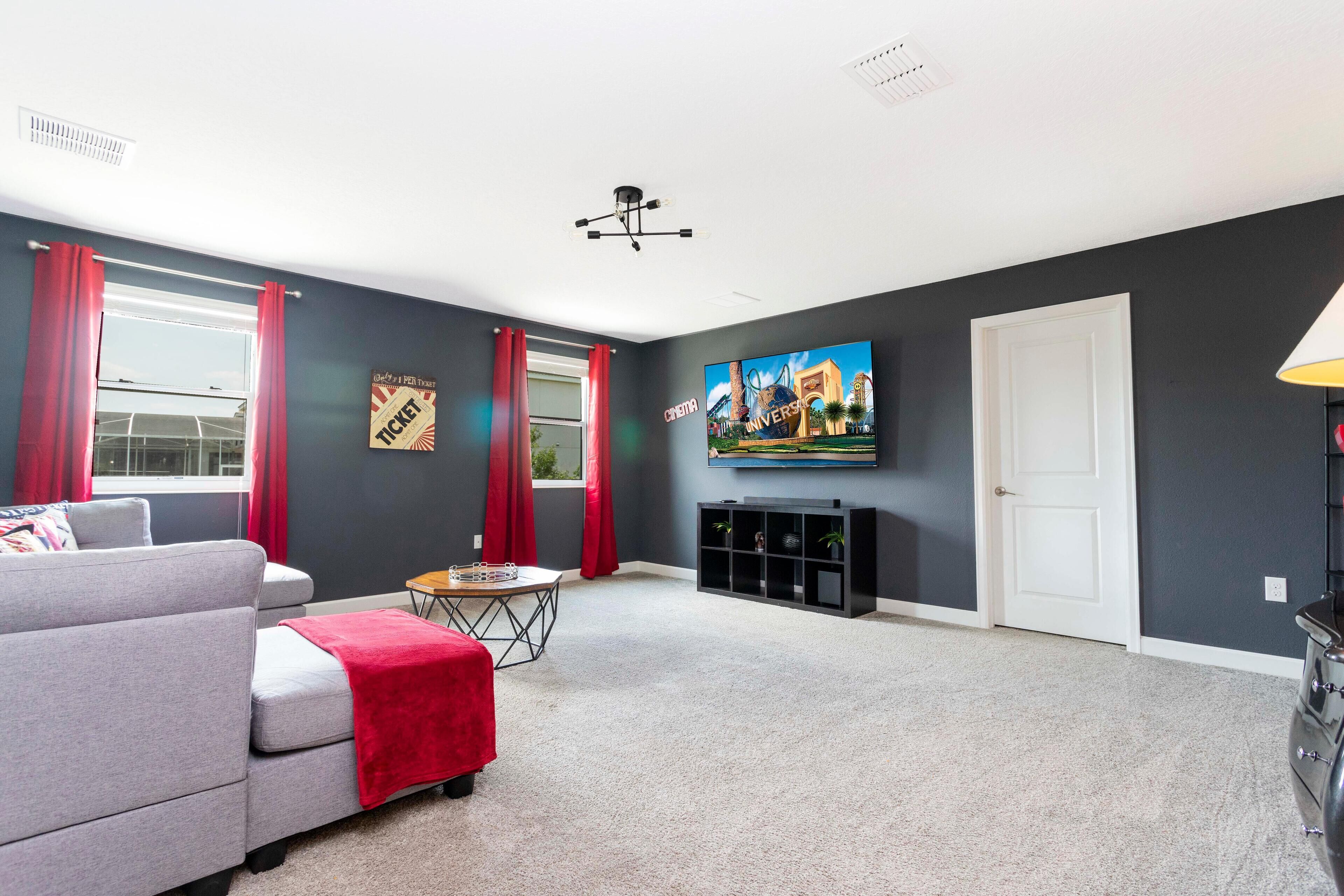 A modern living room with a grey sofa, red curtains, a flat-screen TV, and a fireplace.