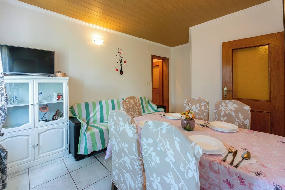 A dining area with a table set for four, a sofa, a cabinet with glass doors, and a television on a cabinet.