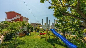 A playground with a blue slide, swings, and a small tree. - Apartments Lino (Lopar)