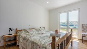 A bedroom with a wooden bed, a desk with a lamp, and a view of a hill through a glass door. - Apartments Lino (Lopar)
