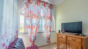 A room with a bed, a TV on a wooden cabinet, and a window with floral curtains. - Apartments Lino (Lopar)