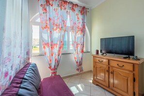 A room with a bed, a TV on a wooden cabinet, and a window with floral curtains. - Apartments Lino (Lopar)