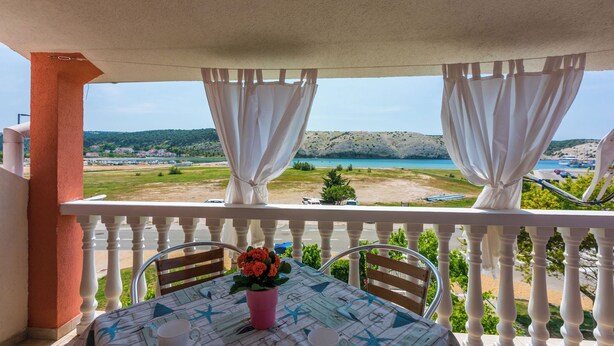 A balcony with a table, chairs, and a view of a beach and water. - Apartments Lino (Lopar)