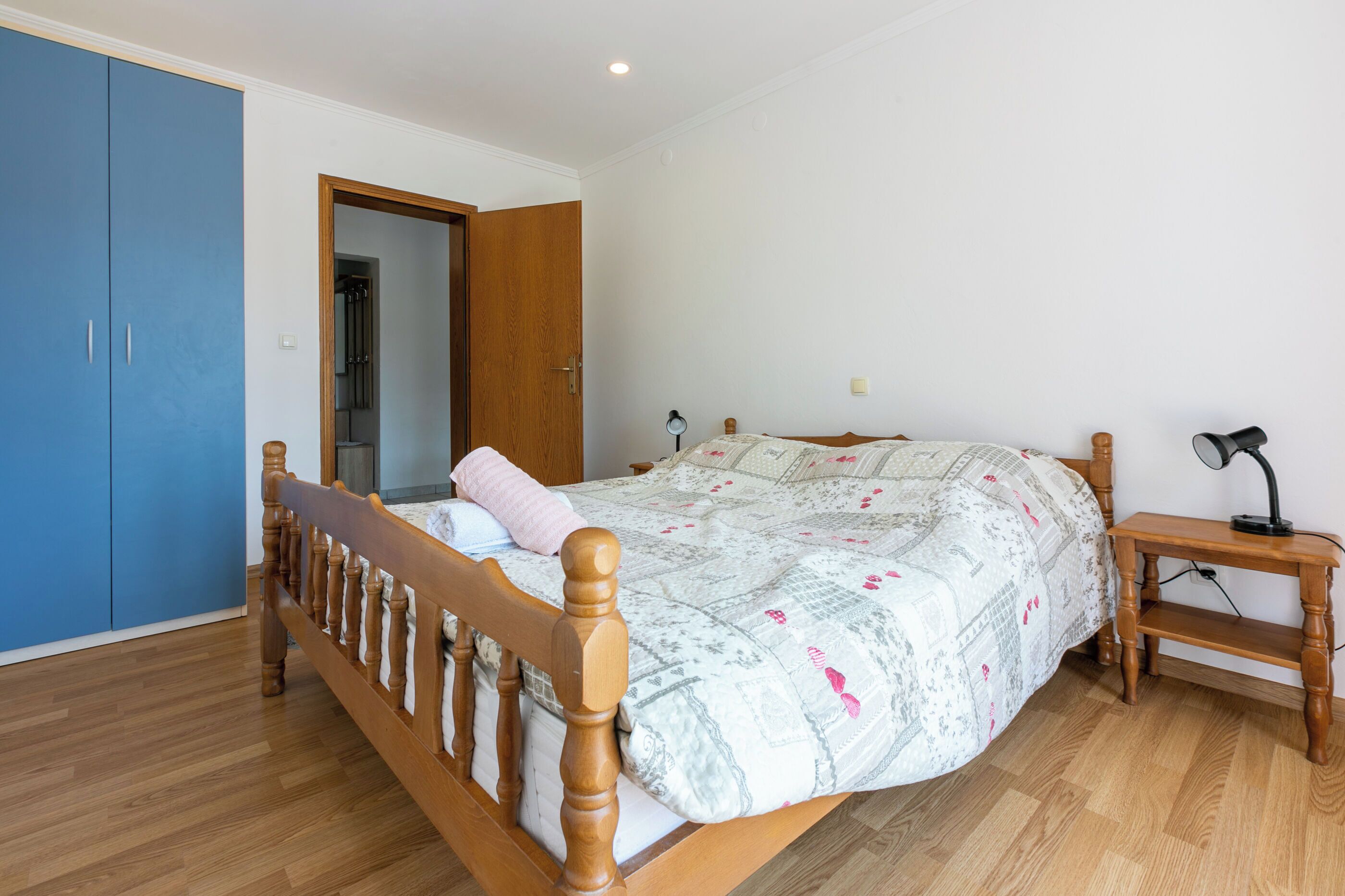 Een slaapkamer met een houten bed, een blauwe garderobe en een bureau met een lamp.